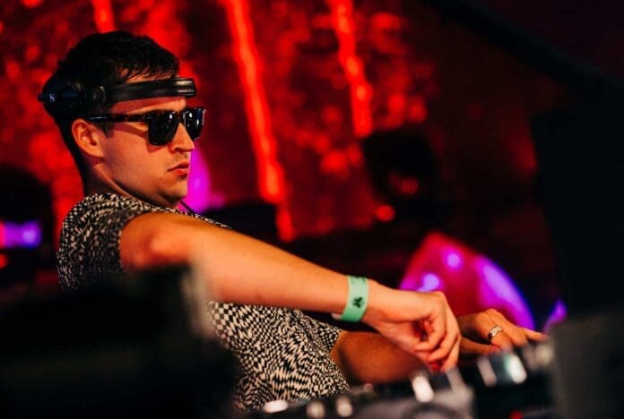 A DJ wearing sunglasses at a party while playing John Summit's 'Fade Out' track featuring MKLA.