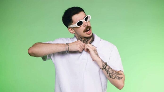 A man with tattoos adjusting his shirt on a green background.