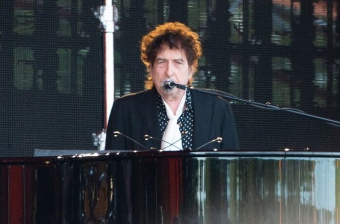 Bob Dylan performing at the Bob Dylan Center during the Universal Publishing Present Songwriter Fellowship, playing a piano and singing into a microphone.