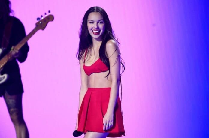 Olivia Rodrigo performs on stage in a red skirt and top.