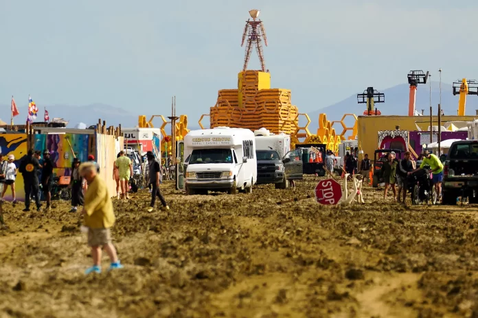 A group of people participating in the Burning Man festival walking down a muddy road.