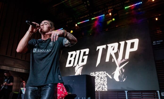 A man singing into a microphone in front of a big sign.