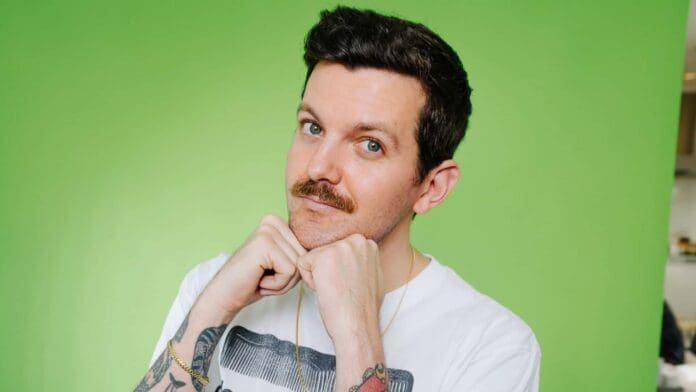 A man with tattoos posing in front of a green background, 