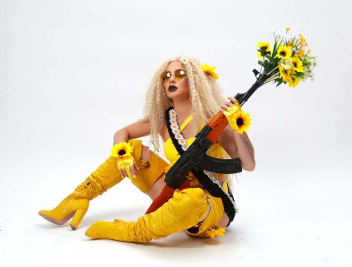 A woman wielding a gun and sunflowers exudes defiance in Eriel Indigo's empowering production 