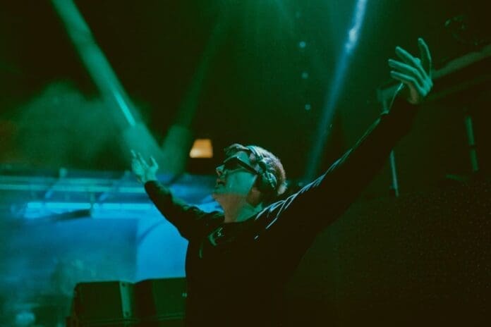 A man with his arms up at a concert experiencing an immersive and cinematic techno atmosphere.