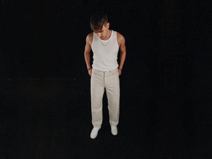 A man in a white tank top standing on a black background.