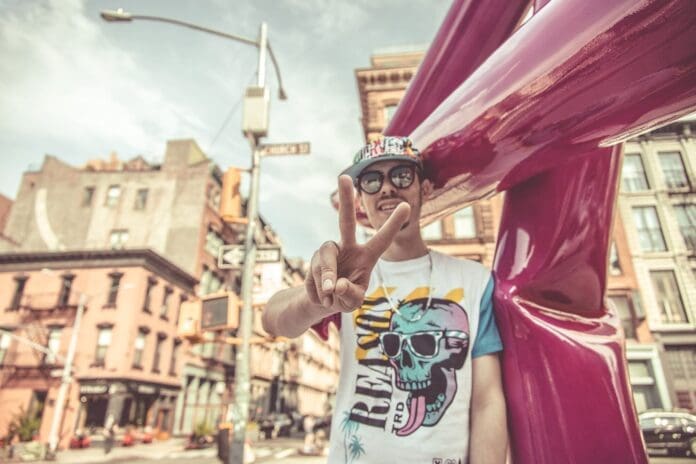 A man wearing sunglasses and a t-shirt poses in front of a pink balloon, vibey house mix.