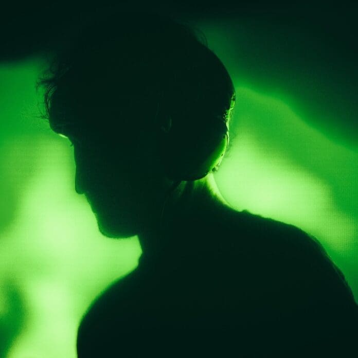 A silhouette of a man with headphones in front of a green light listens to RL Grime's refreshing track 'Borderline'.