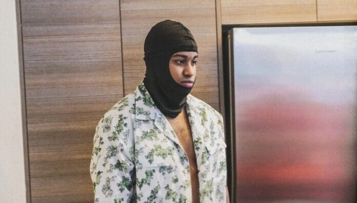 A man wearing a hoodie standing in front of a refrigerator while listening to 