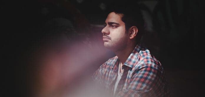 A man sitting in front of a powerful graffiti wall.