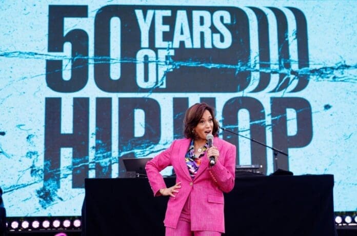 Vice President Kamala Harris celebrates the 50th anniversary of hip-hop, hosting an event with a woman in a pink suit and a sign.