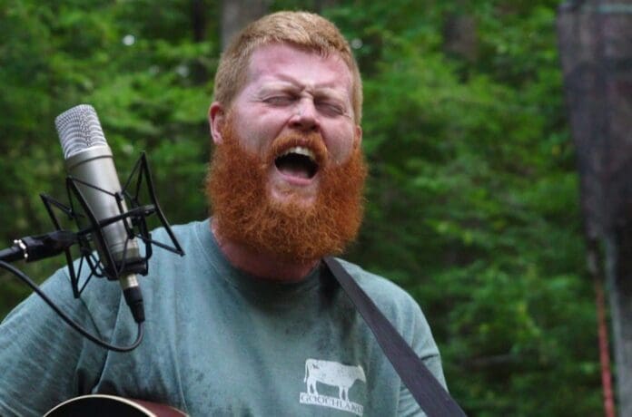 A man singing into a microphone with red beard.