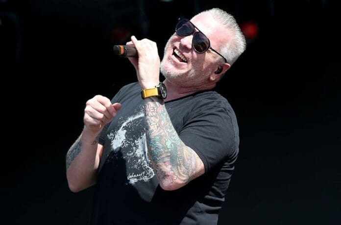 Smash Mouth singer with tattoos singing into a microphone.