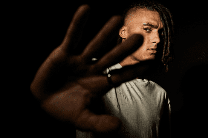 A man with dreadlocks poised in front of a dark background.