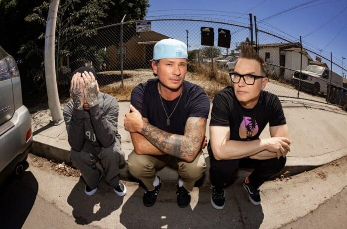 Three men sitting on a sidewalk with tattoos while discussing Blink-182's upcoming North America tour dates.