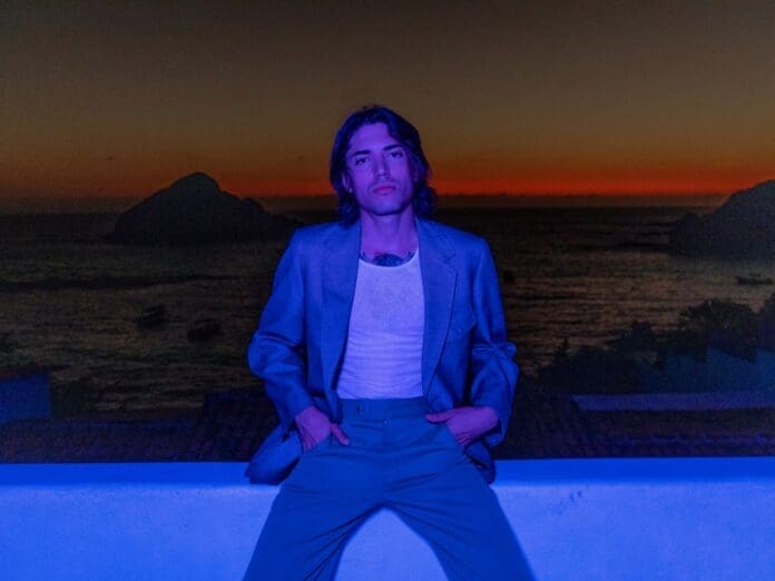 A Sinego man in a suit sitting on a ledge near the ocean.