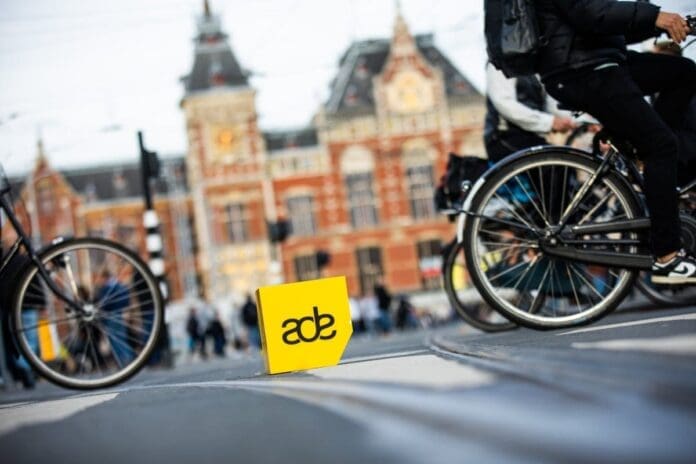 A group of people riding bicycles in front of a yellow sign at Amsterdam Dance Event.