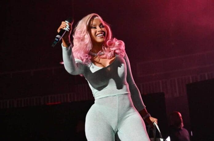 Cardi B in a pink jumpsuit singing on stage.