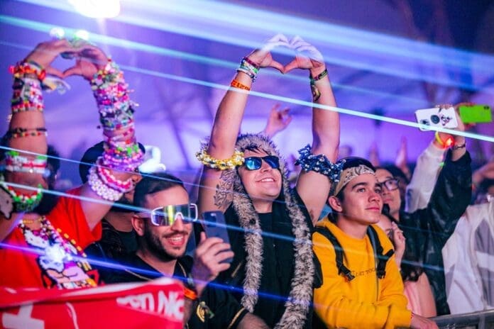 A group of people at a Dreamstate SoCal music festival with their hands up.