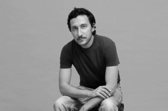 A black and white photo of a man sitting on a stool, emphasizing style.