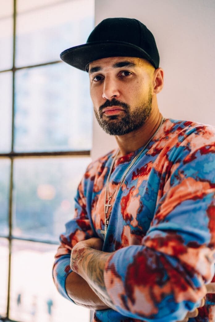 A man wearing a floral shirt standing in front of a window, grooving to OFFAIAH's new tech house gem titled 'Tempo'.