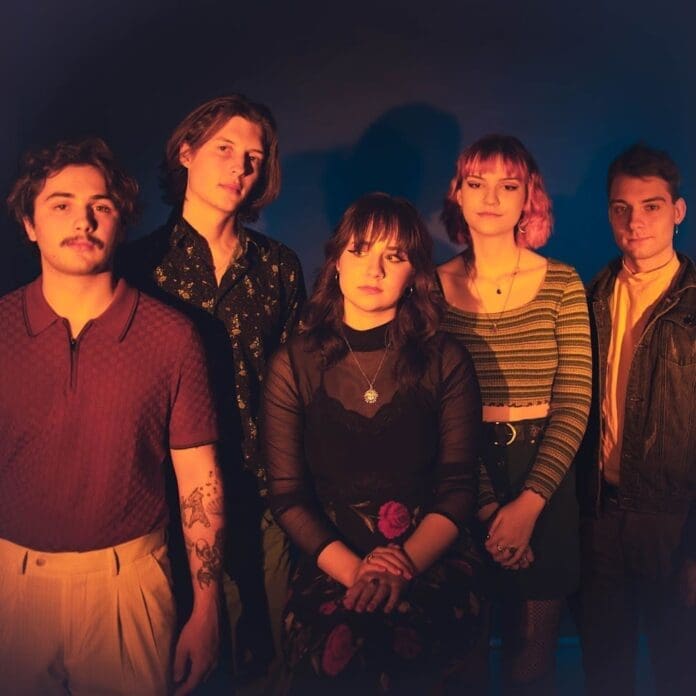 A group of people posing in front of a blue background, sharing their latest new single.