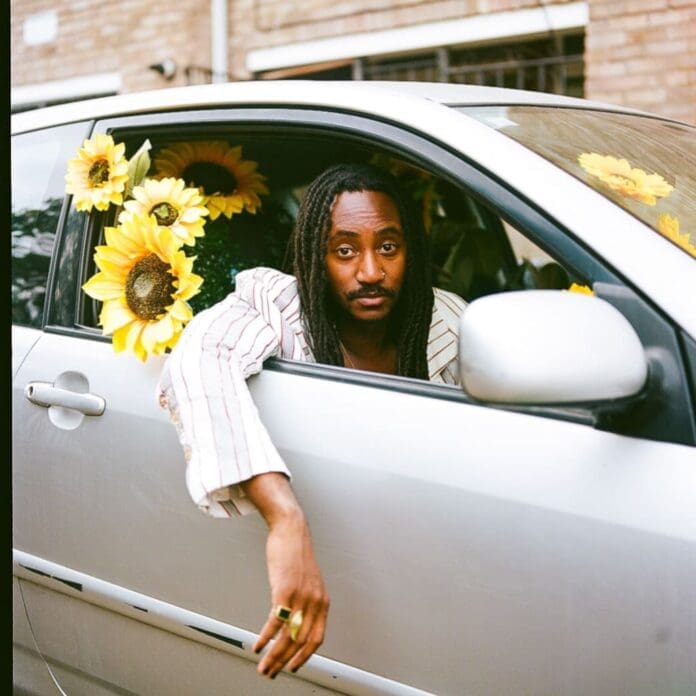 A man leaning out of the window of a car with sunflowers, Seye Adelekan is back with his latest track 