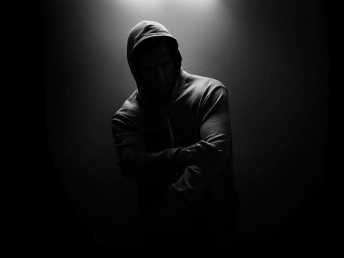 A man in a hoodie standing in the dark unveils 