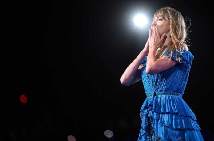 Taylor Swift performs on stage in a blue dress with flowers.