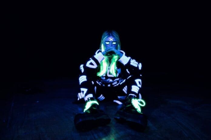 A person sitting on the ground in a glow in the dark outfit for '24 HRS' music video.