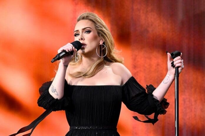 Adele performs on stage in a Halloween-themed black dress.