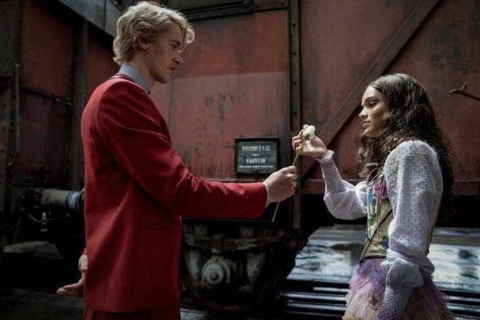 Inside the Music of ‘Songbirds & Snakes’, a man and woman in a red suit standing next to a train.