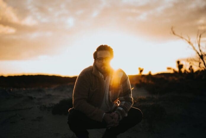 A man crouching in the sand at sunset while Seth Glier shares evocative new single 