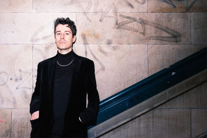 A man in a black jacket standing next to a staircase, captured during Berghain Nights.