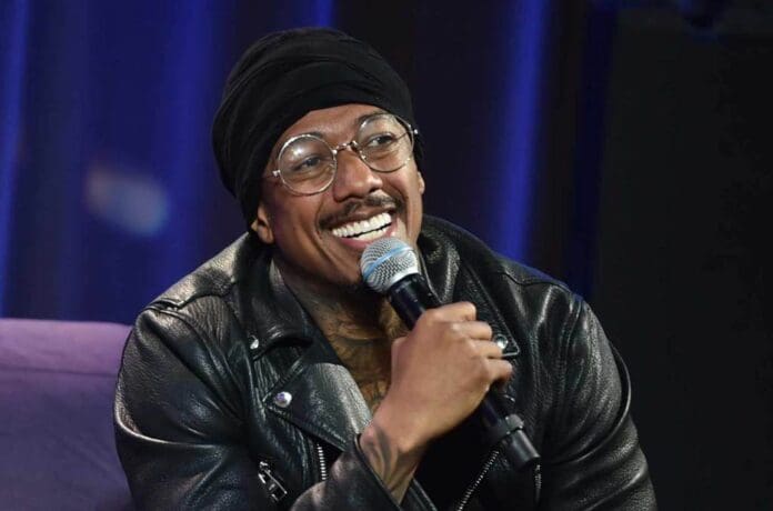 Nick Cannon, wearing a black jacket and hat, is smiling into a microphone as he discusses his holiday plans.