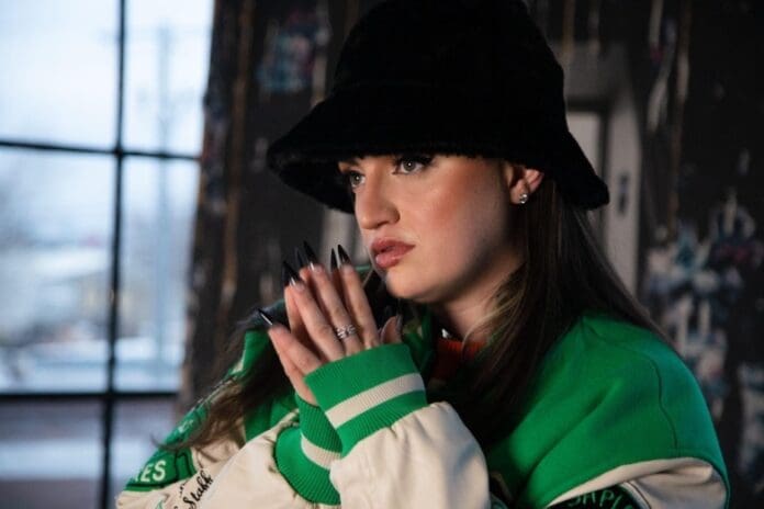 A woman in a green jacket and hat is holding a cell phone while recording a video for Halloween.