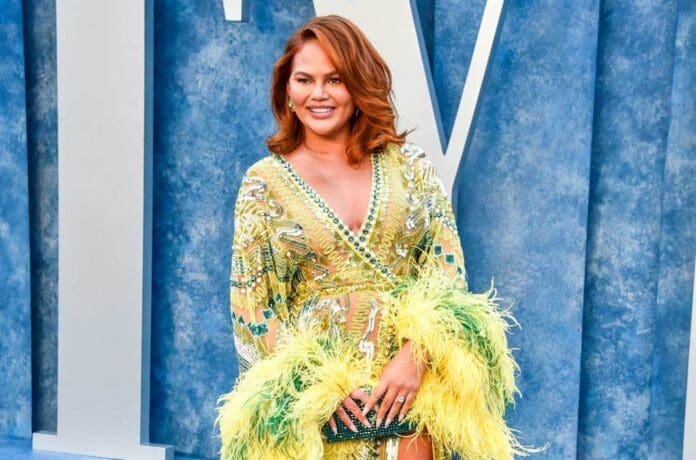 Chrissy Teigen in a yellow dress and feathers on the red carpet.