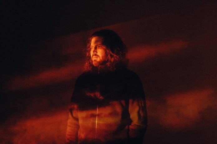 A man with long hair announces the North America Tour standing in front of an orange light.