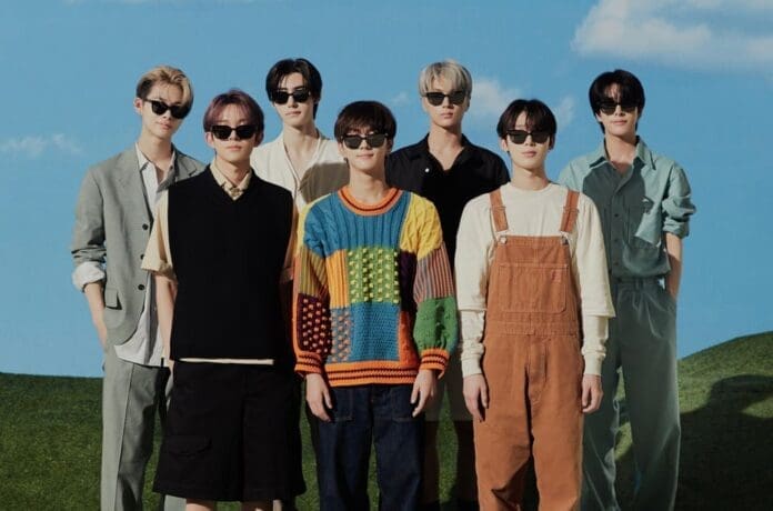 ENHYPEN, a group of young men, posing in front of a grassy field.