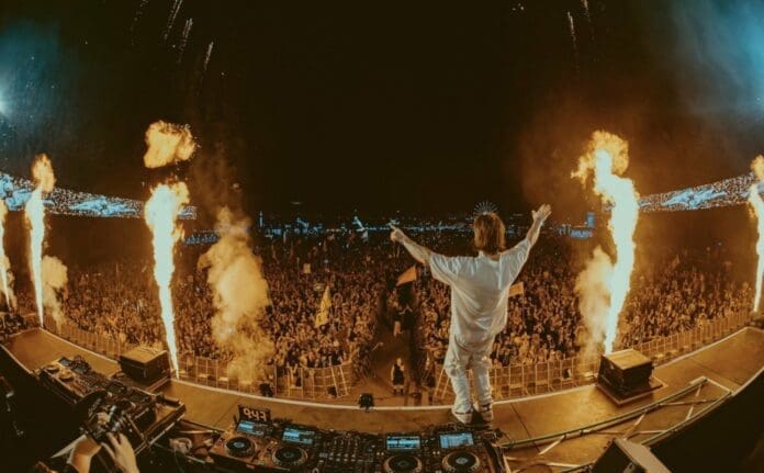 Monstercat DJ standing on top of a stage, with fire in the background.