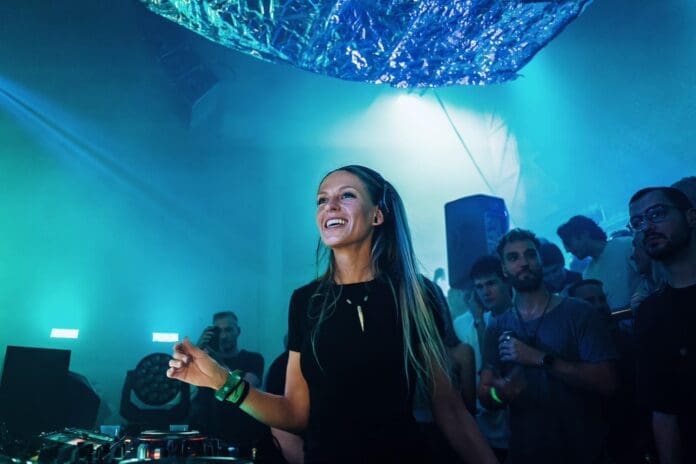 A woman, Nora En Pure, is standing in front of a crowd of DJs while creating mesmerizing illusions through her music.