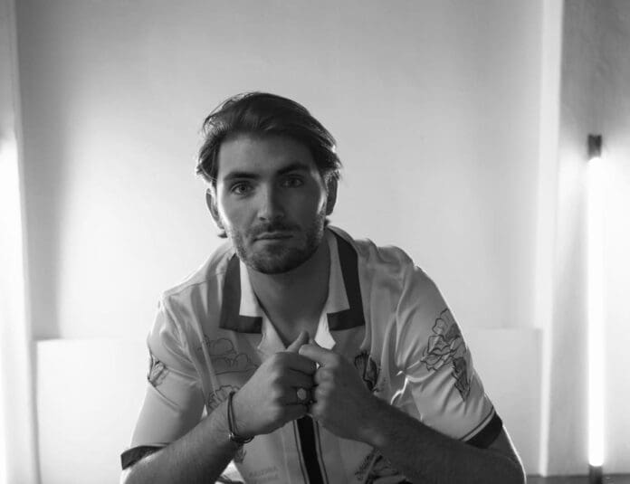 Lukas Vane sitting on a bed at night, wearing a white shirt.