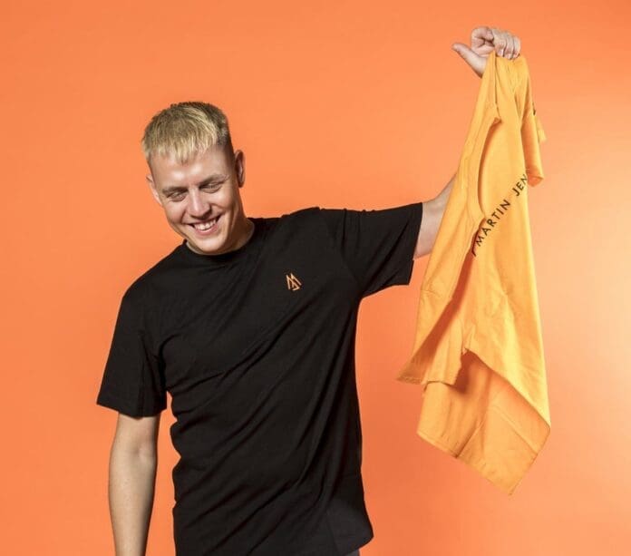 Martin Jensen holding up a t-shirt on an orange background.