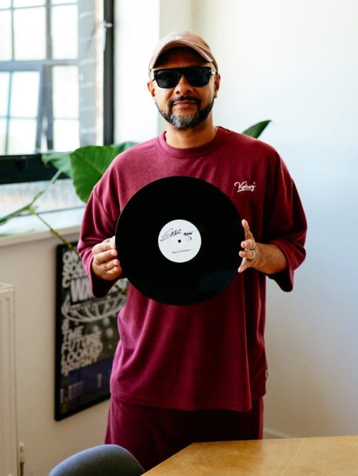 A man holding up a record from Warp Records in front of a window.