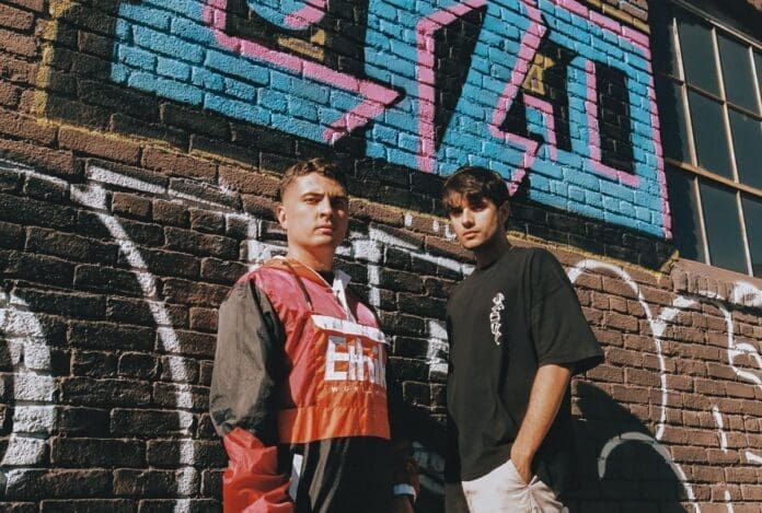 Two young men standing in front of a brick wall adorned with mesmerizing graffiti.