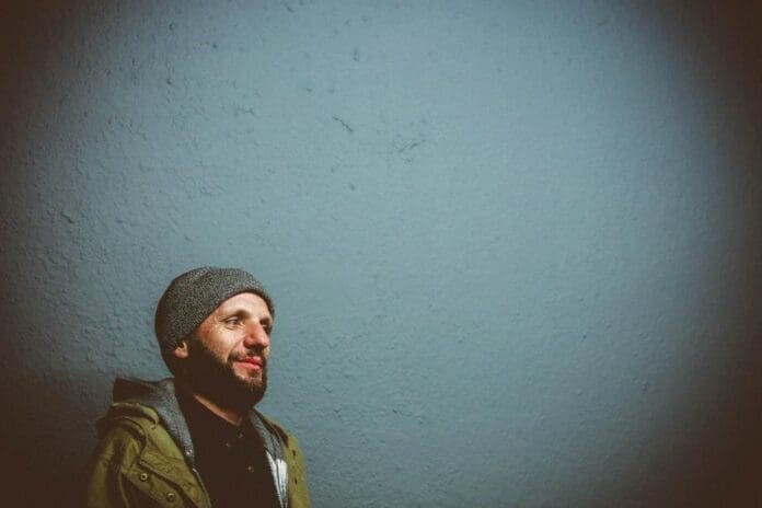 Frank Rabeyrolles, a man in a beanie, standing in front of a blue wall.