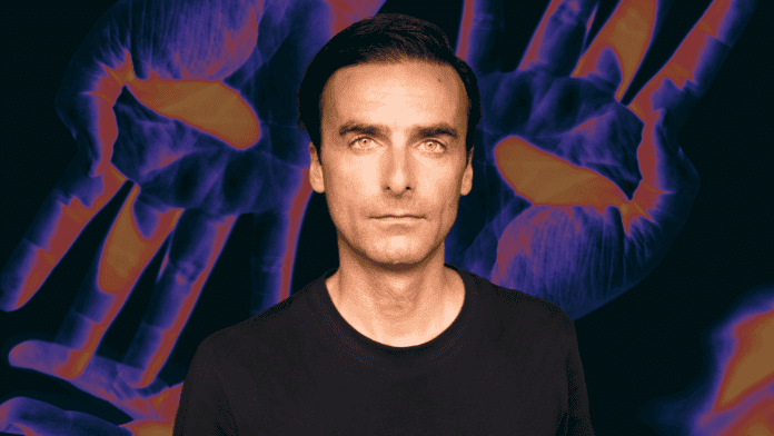 A man is standing in front of a futuristic twist purple and orange background.