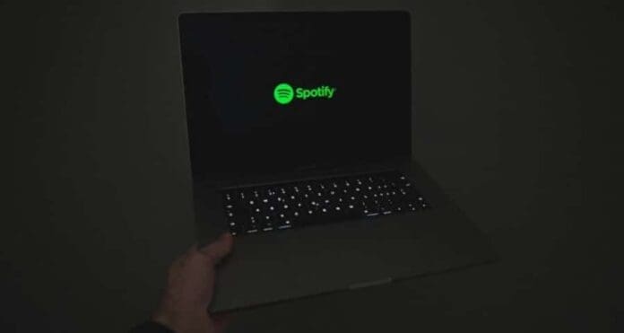 A person holding a laptop with the Spotify logo on it, showcasing artist payments and SEO keywords for starting 2024,000 streams.