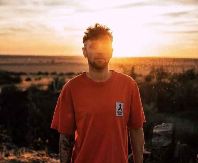 A man in a red t-shirt standing in a field at sunset, captured on the cover of Lexer's debut album 