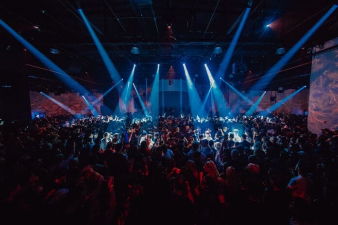 A vibrant crowd of people at a nightclub illuminated by bright lights during New Years Week.